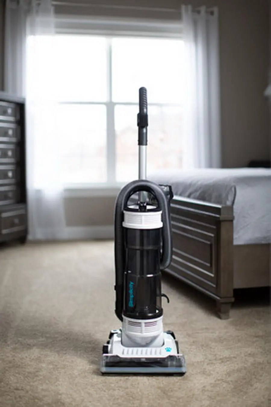 Simplicity S20PET Symmetry bagless upright vacuum in black and white, standing in a bedroom.