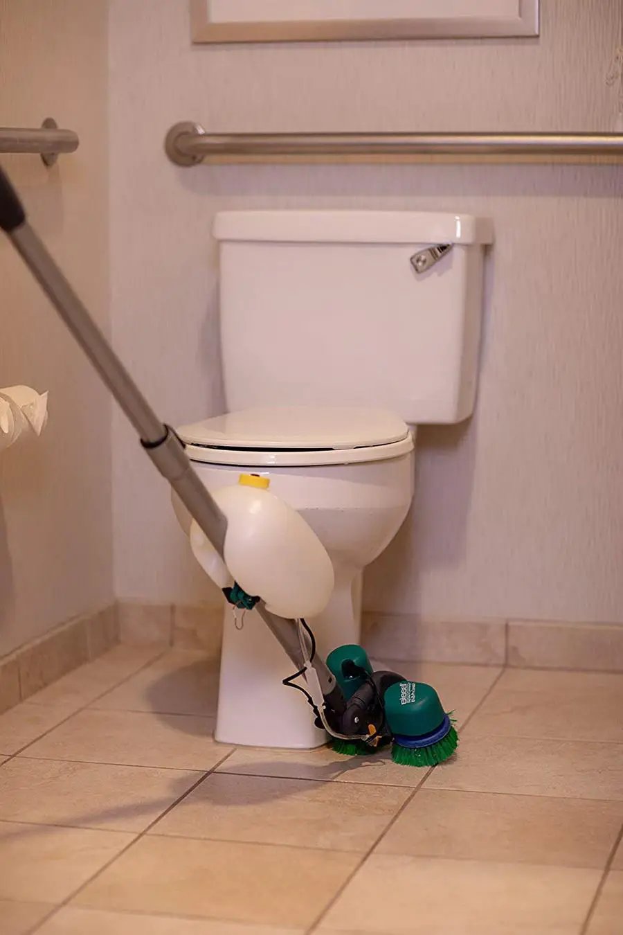 Bissell BGCC1000 dual brush floor machine with green brushes on a tile bathroom floor beside a toilet.