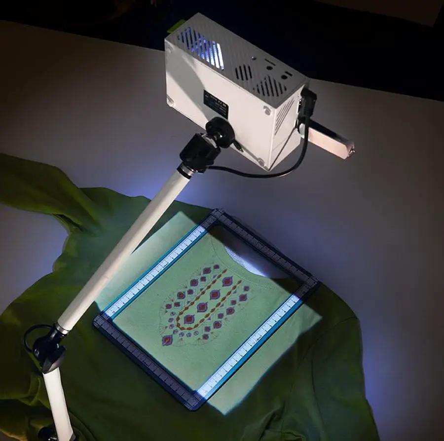 DIME Maximum View Projector on a white adjustable stand projecting onto green patterned fabric
