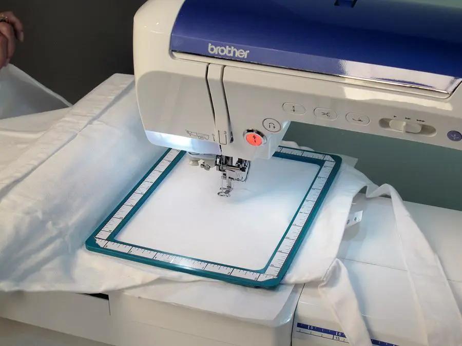 Embroidery machine with blue top, fabric in a square hoop; Brother brand visible