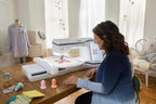 Brother Stellaire Innov-is XE1 embroidery machine, white with blue accents, on a wooden table.