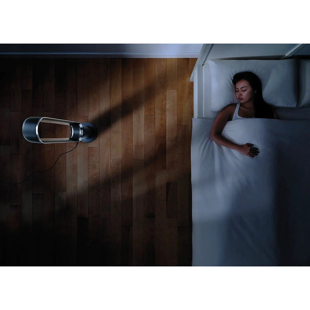 Dyson AM07 Tower Fan in black on a wooden floor beside a bed.