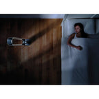 Dyson AM07 Tower Fan in black on a wooden floor beside a bed.