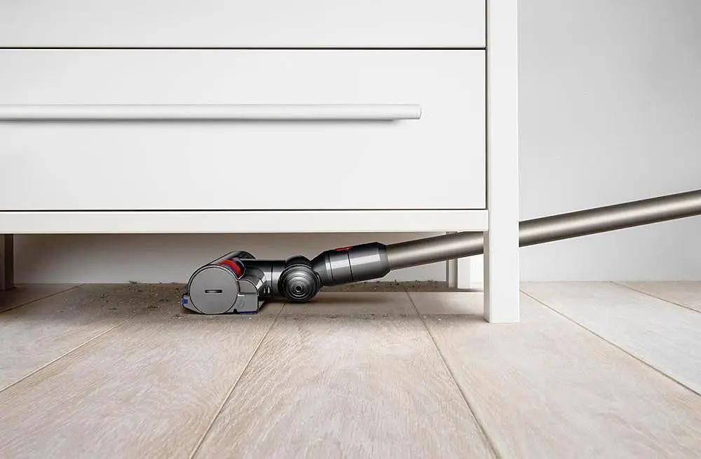 Dyson V8 Animal cordless vacuum under cabinet with long wand; gray body with red accents.