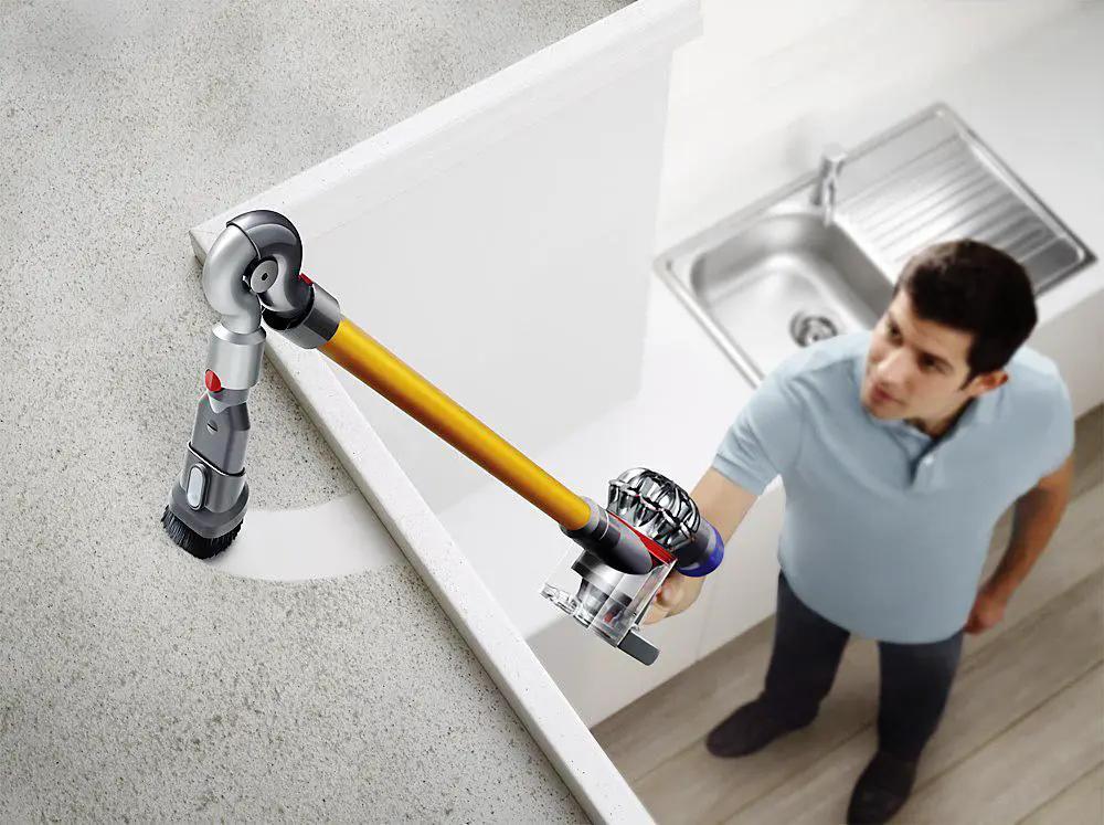 Dyson V8 Absolute cordless stick vacuum with yellow wand and silver body cleaning near a kitchen sink