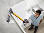 Dyson V8 Absolute cordless stick vacuum with yellow wand and silver body cleaning near a kitchen sink