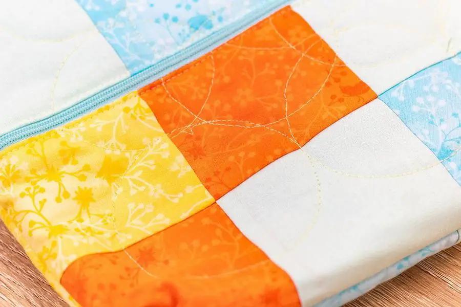 Gemini 6-in-1 Quilting Pattern Guide Set 1; orange-yellow patchwork fabric with blue zipper.