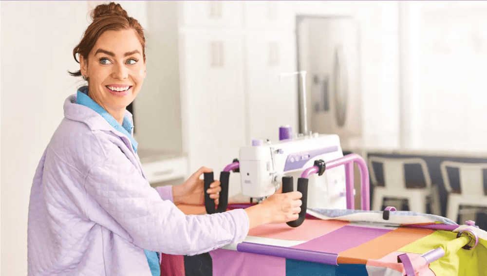 Handi Quilter FreeWay Quilt Frame in purple and white, shown in use by a smiling quilter.
