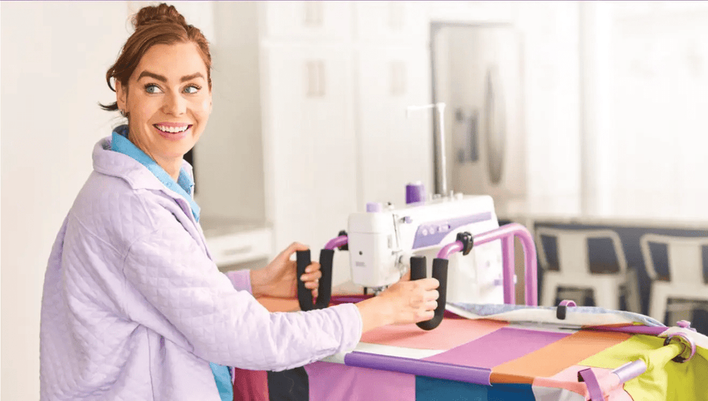 Handi Quilter FreeWay Quilt Frame in purple and white, shown in use by a smiling quilter.
