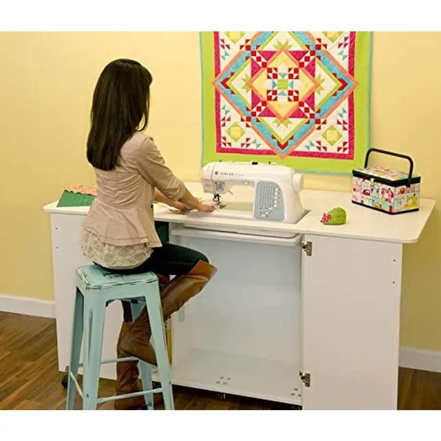 Kangaroo Kabinets Emu sewing cabinet in white with a sewing machine; person seated on a light blue stool at a sewing table.