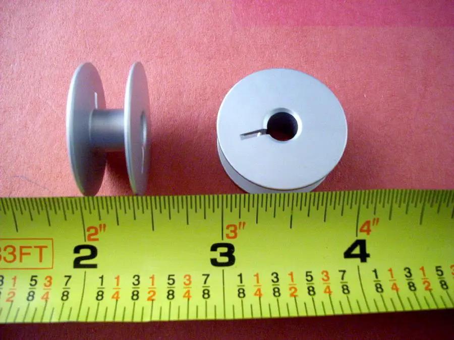 Two gray aluminum bobbins with slot, Large M, Superior brand, shown with a ruler for scale
