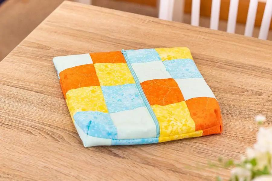 Quilting pattern guide set in a colorful patchwork quilted pouch with teal zipper on a wooden table