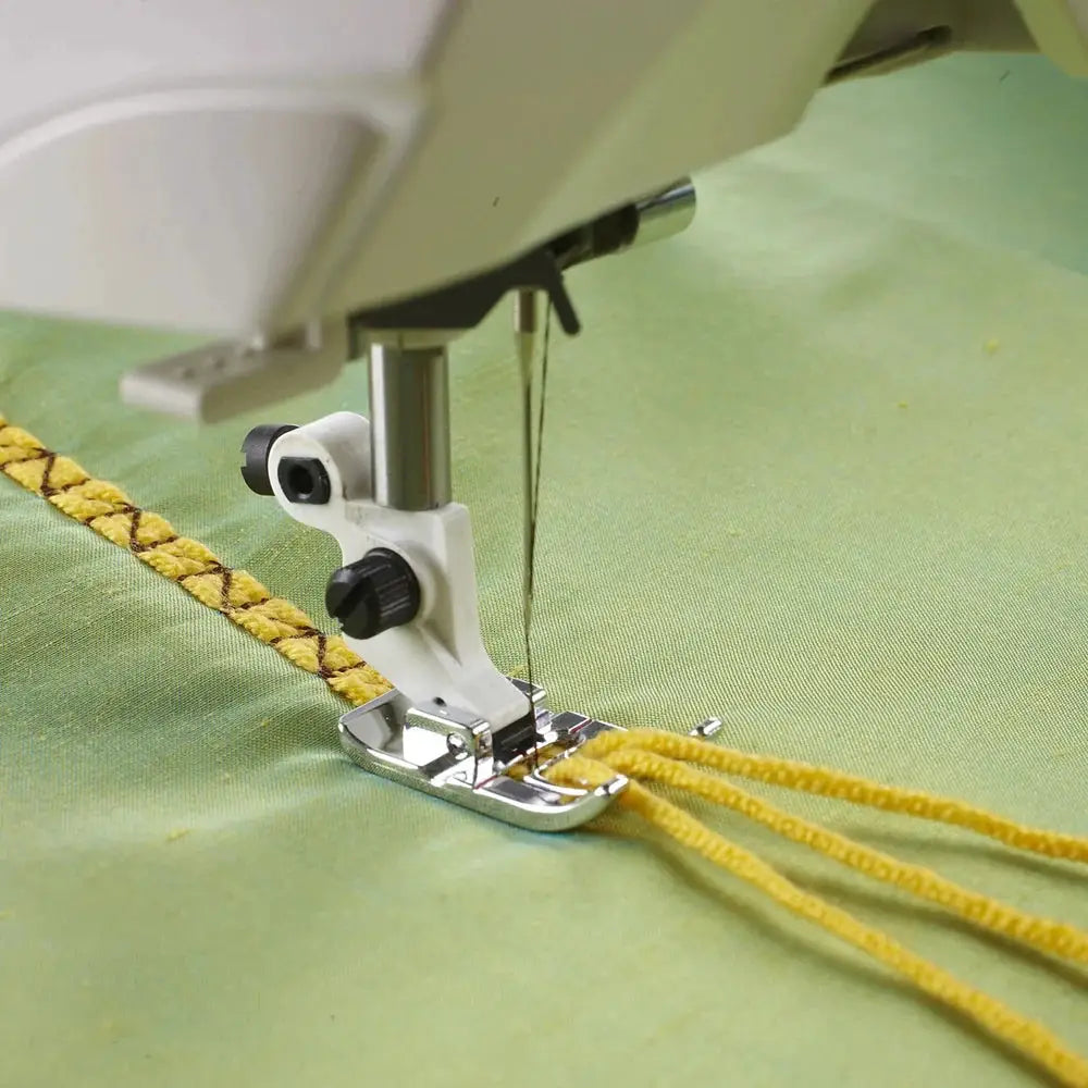 Husqvarna Viking Three-Hole Yarn Foot presser foot on green fabric guiding yellow yarn