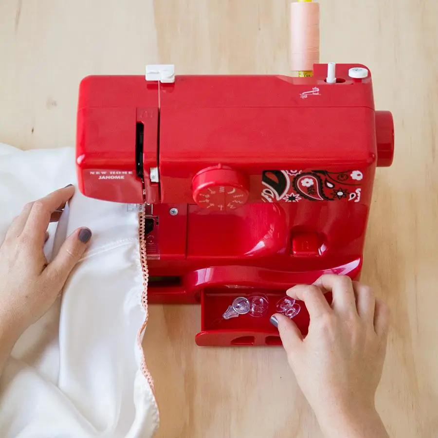 Janome Derby Line portable sewing machine in bandana blush red; hands guiding fabric under needle.