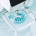 Sew Tech 80mm x 80mm embroidery hoop on light blue fabric with teal embroidery.