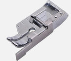 A polished silver metal 1/4" patchwork quilting foot on a plain light gray background w/ guide.