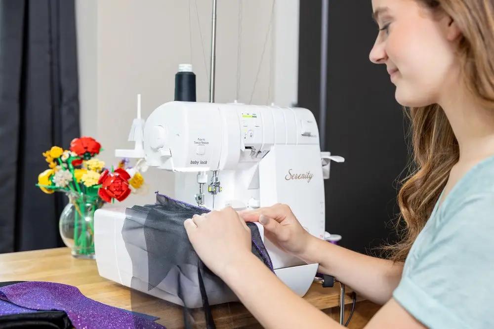 Baby Lock Serenity 4-Thread Serger sewing machine in white with user guiding purple fabric.