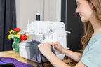Baby Lock Serenity 4-Thread Serger sewing machine in white with user guiding purple fabric.