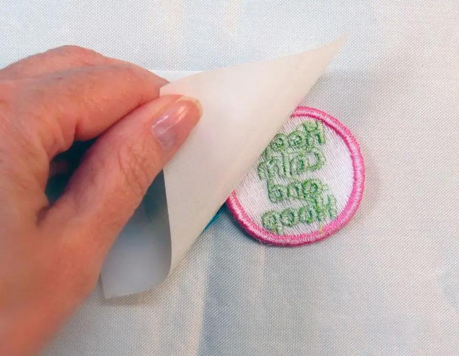 Stabilizer bundle from DIME: hand peeling clear backing to reveal a pink-edged embroidered patch