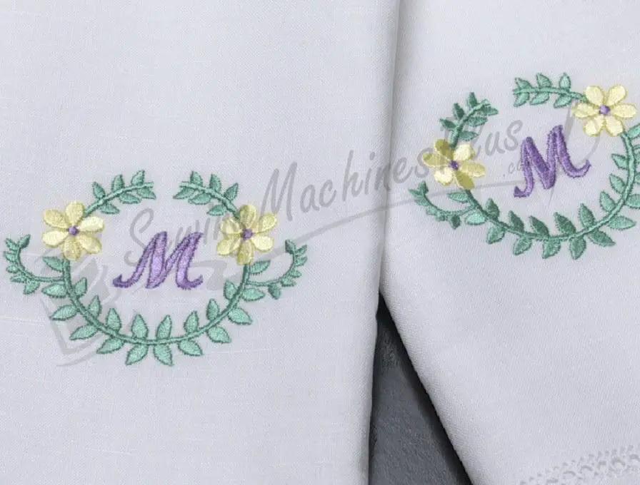 Singer S10 Studio embroidery on white fabric showing two green leaf wreaths with purple M monograms