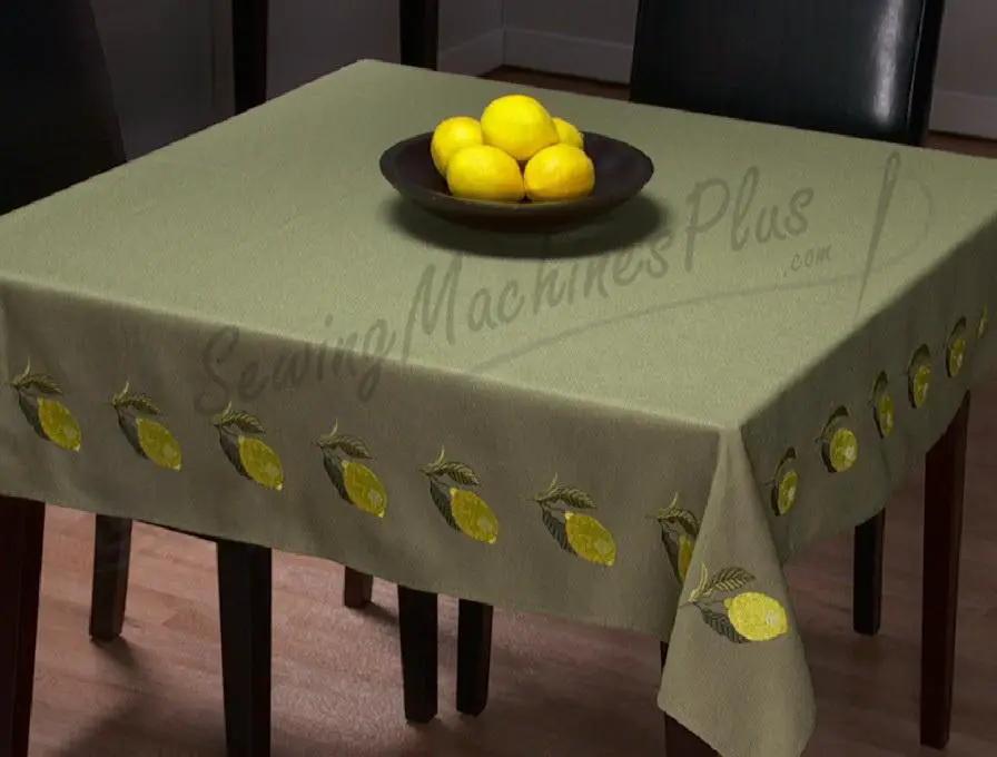 Green lemon-pattern tablecloth on a dining table with a bowl of lemons and chairs in the background.