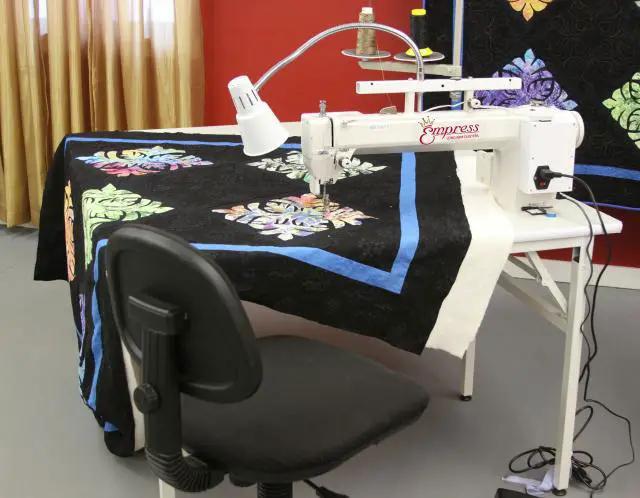 Tin Lizzie Empress sit-down long-arm quilting machine, white on a table with a colorful quilt