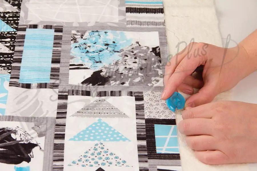 TrueCut TrueTrim Thread Cutter, blue handheld tool used to trim threads on a patchwork quilt.
