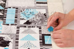 TrueCut TrueTrim Thread Cutter, blue handheld tool used to trim threads on a patchwork quilt.