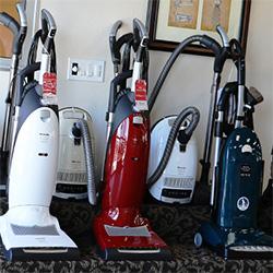 White, red and blue vacuum cleaners are aligned near the wall