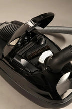 The Bank Vault Canister Vacuum in black with lid open, showing brush roller and hose.