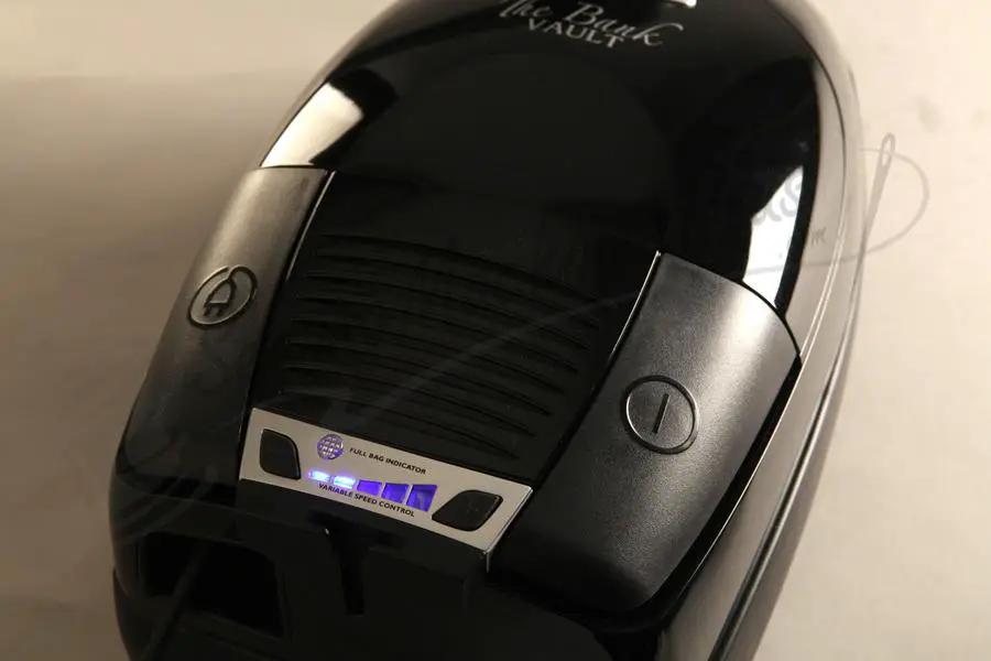 The Bank Vault canister vacuum in black glossy finish with blue indicator lights.